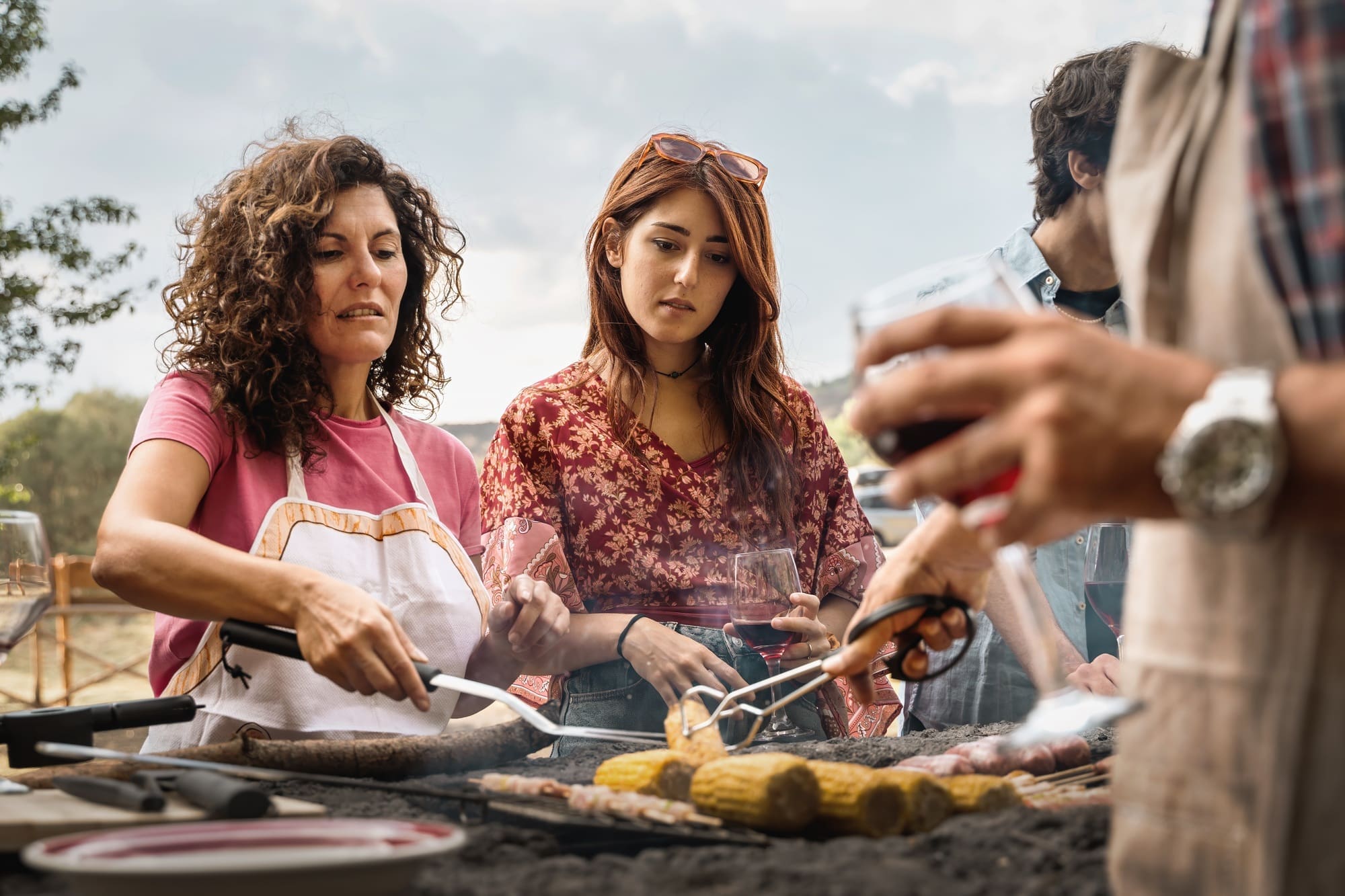 Women grilling food and drinking wine at outdoor barbecue gathering